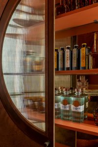 Mueble bar del Espacio SixtyPro en Casa Decor 2026 con vitrina de cristal texturizado, estanterías iluminadas y botellas de LE Tribute integradas en el interiorismo.