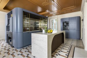 Cocina a medida de Schmidt en Casa Decor 2026 con isla de Dekton Nara, módulos curvos azul grisáceo, electrodomésticos Küppersbusch integrados y suelo de mosaico Hisbalit.