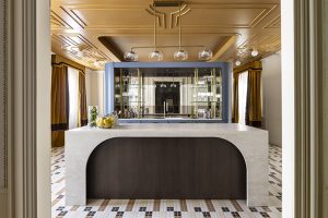 Cocina del espacio “La Unidad” de Schmidt y Lemon Studio en Casa Decor 2026 con isla revestida en Dekton Nara de Cosentino, mobiliario azul a medida y techo albero con molduras Orac.