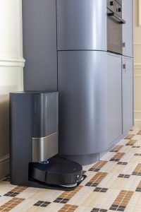 Robot aspirador Dreame integrado junto al mobiliario azul a medida de Schmidt en el espacio “La Unidad”, con suelo de mosaico vítreo Hisbalit en tonos beis y marrones.