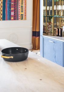 Detalle decorativo de la cocina de “La Unidad” con encimera Dekton Nara, sartén negra con asas doradas, vitrina con perfilería metálica y mobiliario azul de Schmidt.
