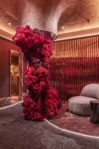 Hall diseñado por Keinzo Interiores en Casa Decor 2026 con revestimientos metálicos Homapal, composición floral escultórica en tonos rojos y mobiliario de formas orgánicas.